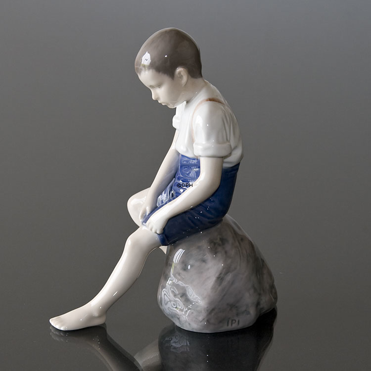 Junge sitzt auf einem Stein und rollt seine Hose auf, Bing & Gröndahl Figur Nr. 1757