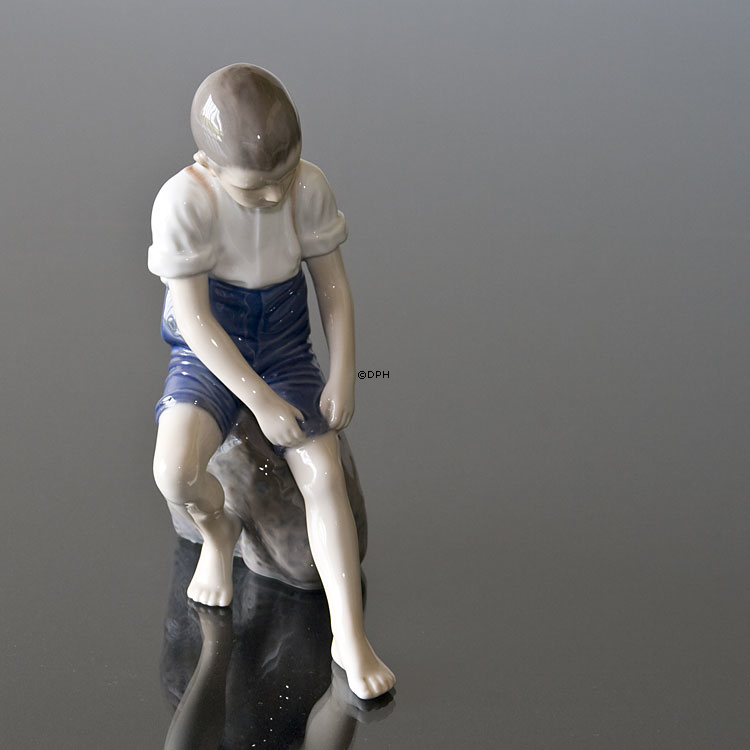 Junge sitzt auf einem Stein und rollt seine Hose auf, Bing & Gröndahl Figur Nr. 1757