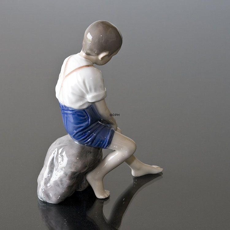 Junge sitzt auf einem Stein und rollt seine Hose auf, Bing & Gröndahl Figur Nr. 1757