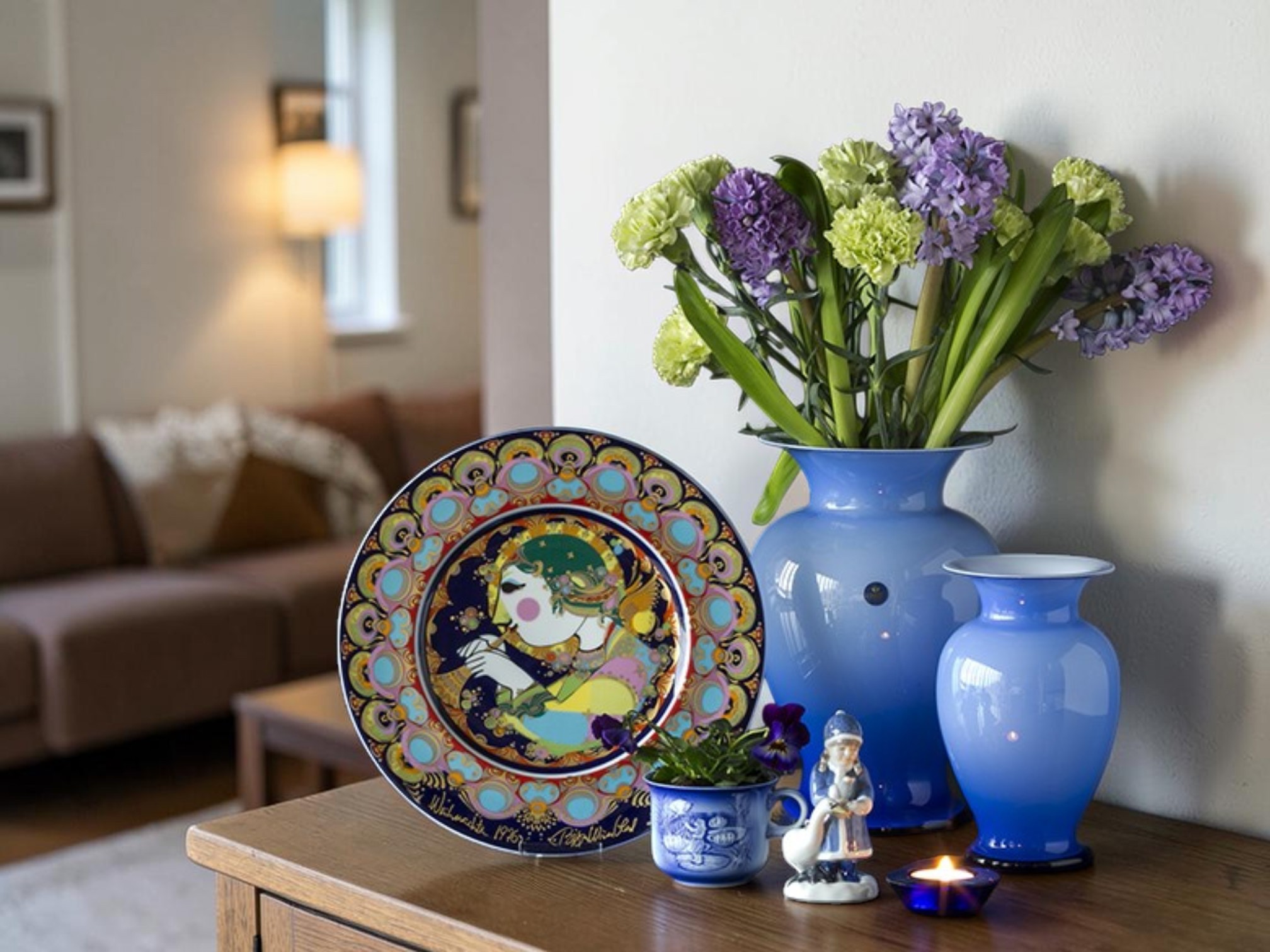 Rosenthal Björn Wiinblad Weihnachtsteller mit farbenfrohem Weihnachtsmotiv ausgestellt auf einer Anrichte zusammen mit blauen Glasvasen und nordischem Wohndesign.