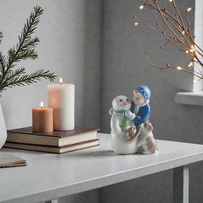 Royal Copenhagen Figur Else baut Schneemann steht auf einem Sideboard mit Tannenzweigen in einer Vase, Kerzen und kleinen warmen Weihnachtslichtern.