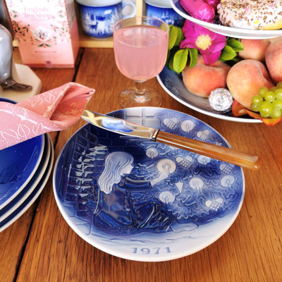 Désirée Weihnachtsteller von 1971 mit einem Hans Christian Andersen Motiv, verwendet auf einer Frühjahrstafel. Der Tisch ist mit einer rosa Serviette, Obst und Kuchen gedeckt und schafft eine gemütliche Atmosphäre.