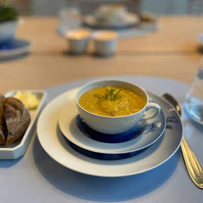 Alte Porzellantasse, die als Suppenschale für die Vorspeise verwendet wird, serviert mit Brot und Butter. Eine kreative und persönliche Tischdekoration.