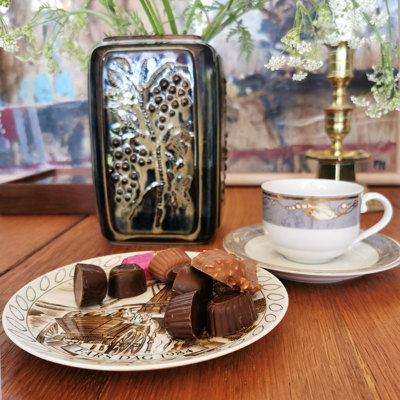 Egemose Vatertagsteller, verwendet als Kuchenteller mit Schokolade, kombiniert mit einer Magnolia Kaffeetasse und einer Vase mit Dekoration im Hintergrund.
