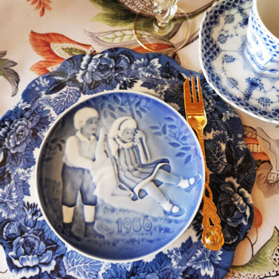 Barnets Dag Teller von 1986, verwendet als Kuchenteller in einer Tischdekoration mit blau gemustertem Service, vergoldeter Kuchengabel und Glas.