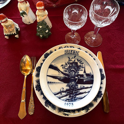 Weihnachtstafel mit einem Hackefors Weihnachtsteller und einem Jenny Nyström Weihnachtsteller, die als Essteller verwendet werden. Der Tisch ist mit Kristallgläsern, Goldbesteck und Else-Figuren als Dekoration geschmückt.