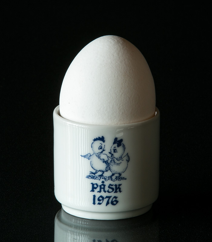 Bunte Ostereierbecher von Rörstrand, Hutschenreuther und anderen, dekoriert mit Frühlingsmotiven wie Hasen und Küken, festlich auf einem gedeckten Ostertisch arrangiert