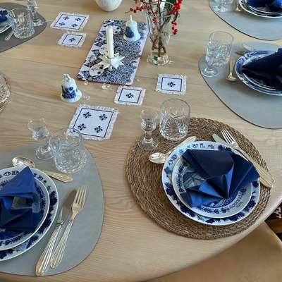 Weihnachtsmittagstafel mit einem Jenny Nyström Weihnachtsteller für den Hauptgang und einem Seltmann Schwedische Landschaften Teller für die Vorspeise. Das Arrangement in Blau- und Weißtönen wird mit einer Serviette und Kristallgläsern abgerundet.