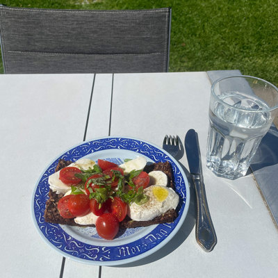 Rörstrand Muttertagsteller, verwendet als Mittagsteller mit Roggenbrot, Mozzarella und Tomaten. Im Garten im Freien mit einem Glas Wasser serviert.